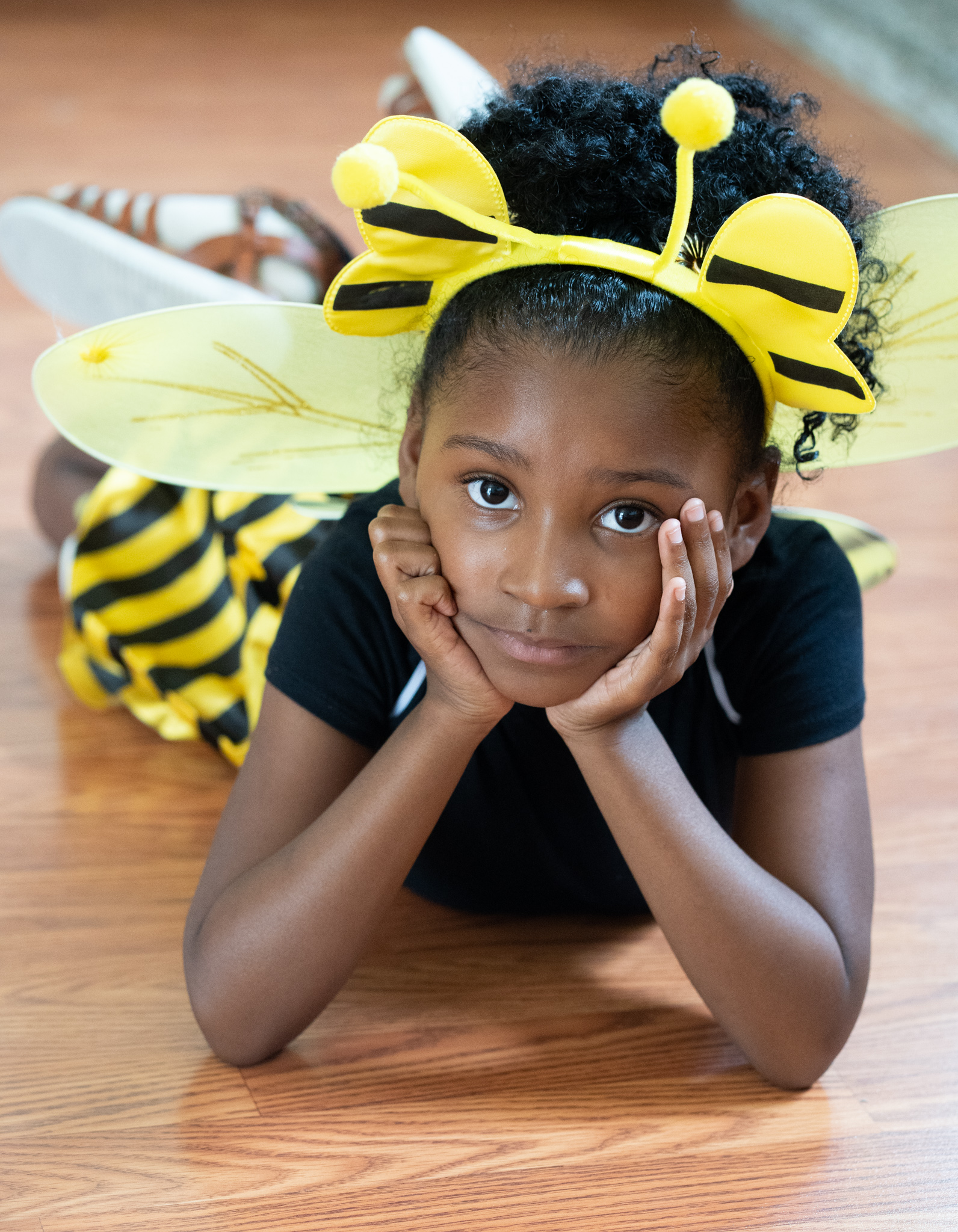 Child wearing a bee costume headband, lying on the floor
